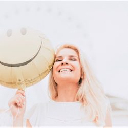 woman smiling and holding a happy face balloon